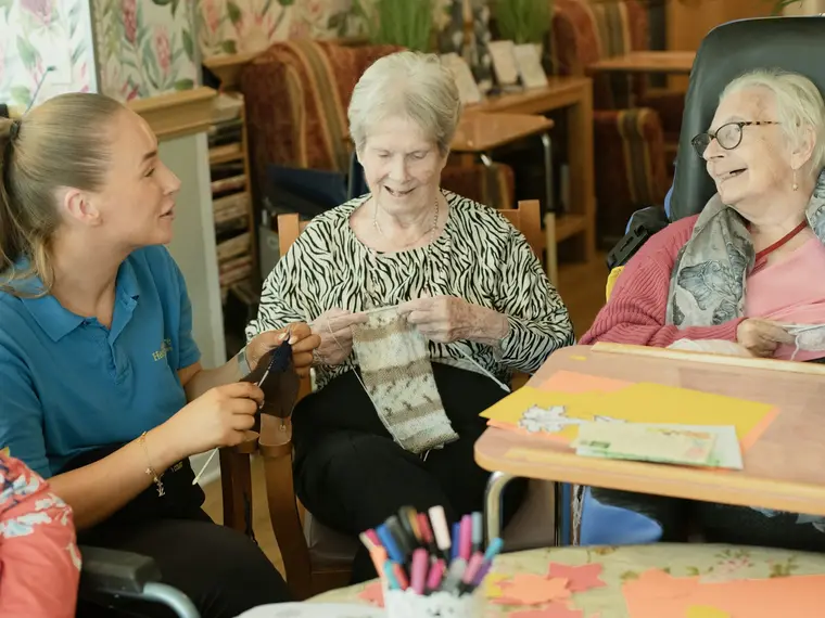 Des résidentes tricotent avec une accompagnatrice dans le salon d'une maison de repos